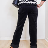 Person wearing a black and white striped sweater and black pants against a white wall.