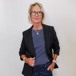 Woman wearing a black pinstripe blazer, blue shirt, and jeans against a white background