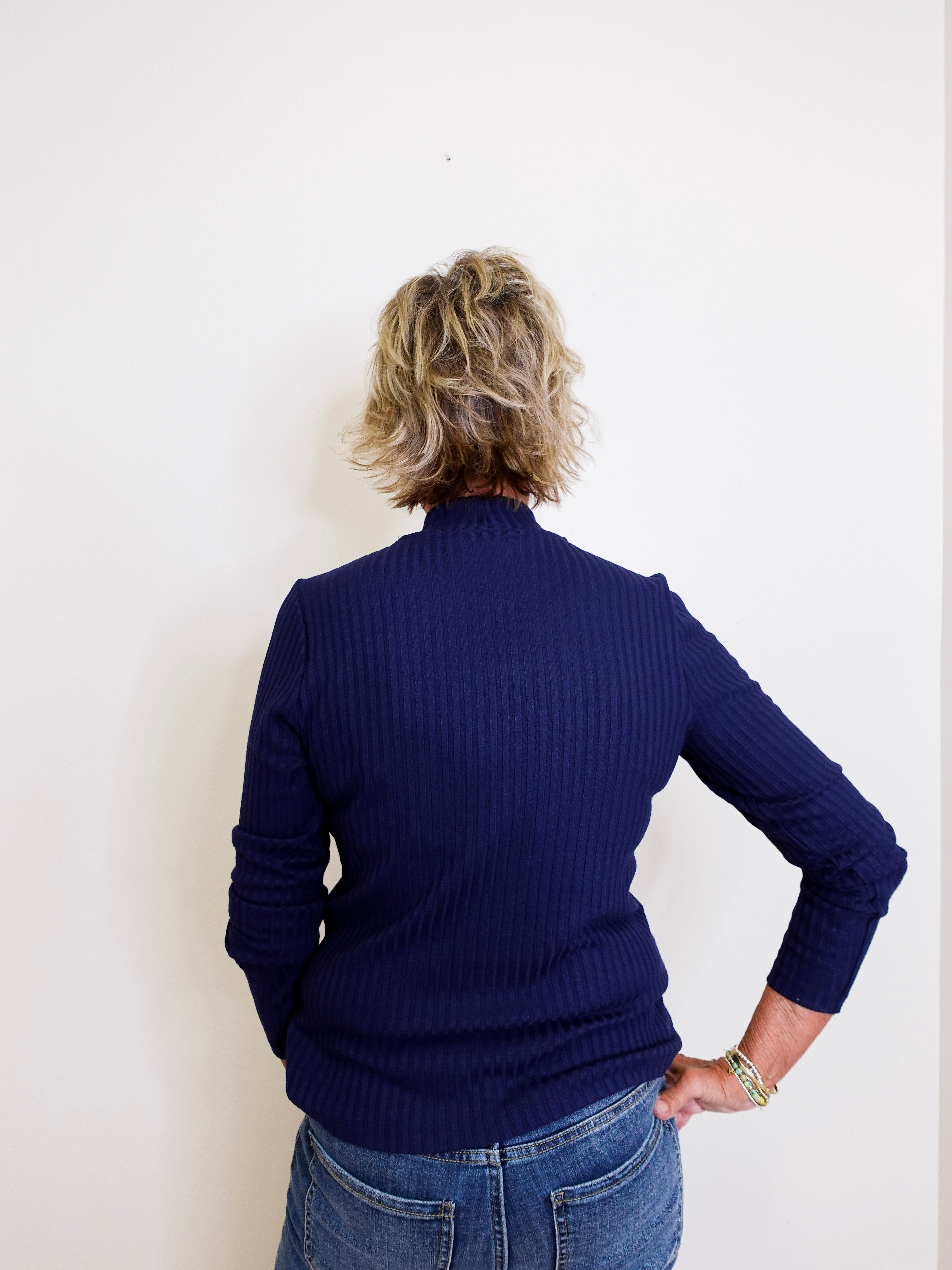 Person wearing a navy blue sweater and jeans against a white background