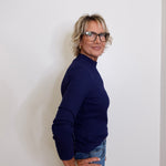 Woman wearing a navy sweater and jeans against a white wall