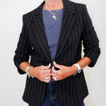 Person wearing a black pinstripe blazer over a blue shirt with a plain background