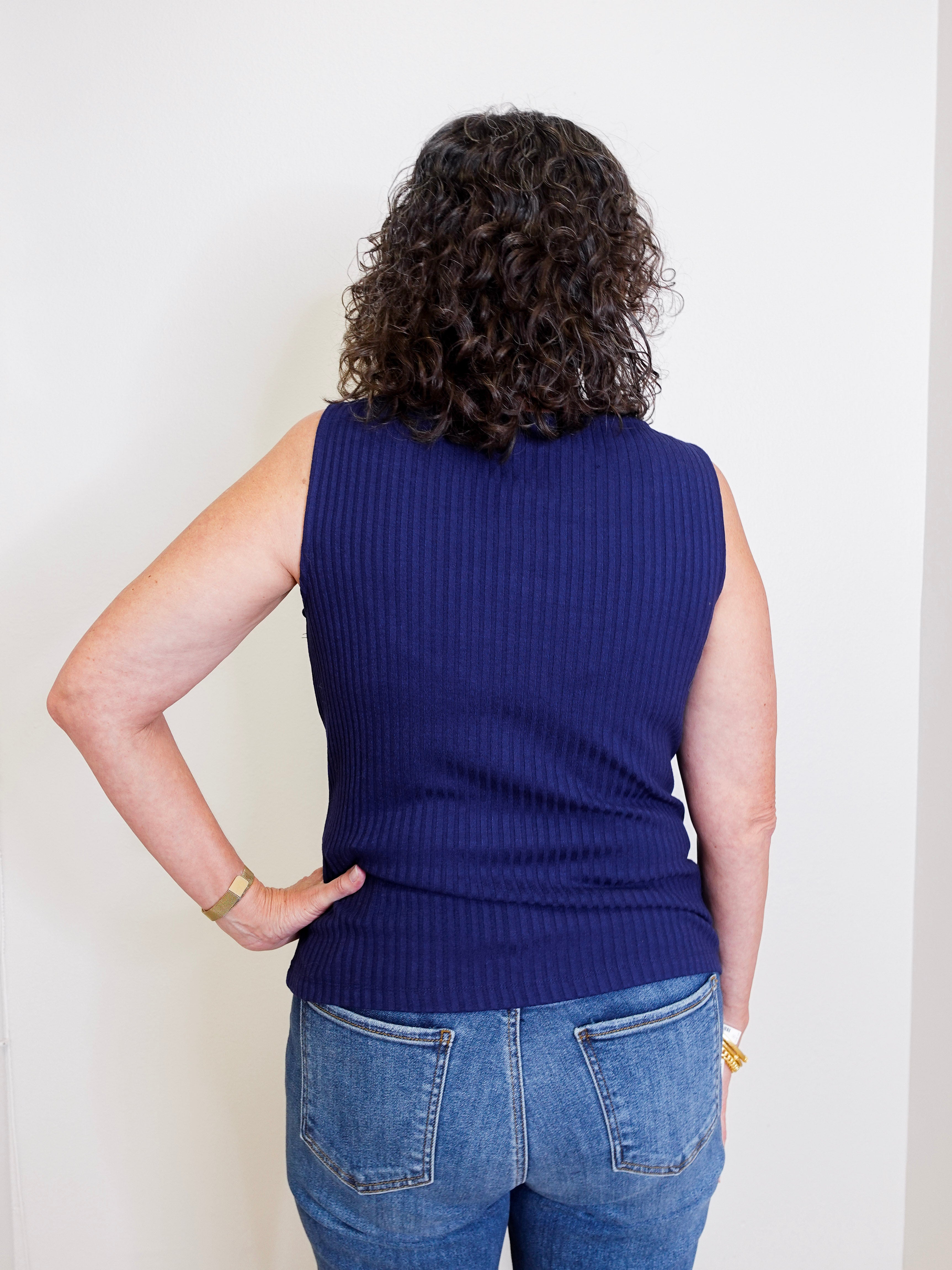 Person wearing a blue sleeveless sweater and jeans against a white background