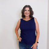 Woman wearing a navy blue sleeveless top and jeans against a white background