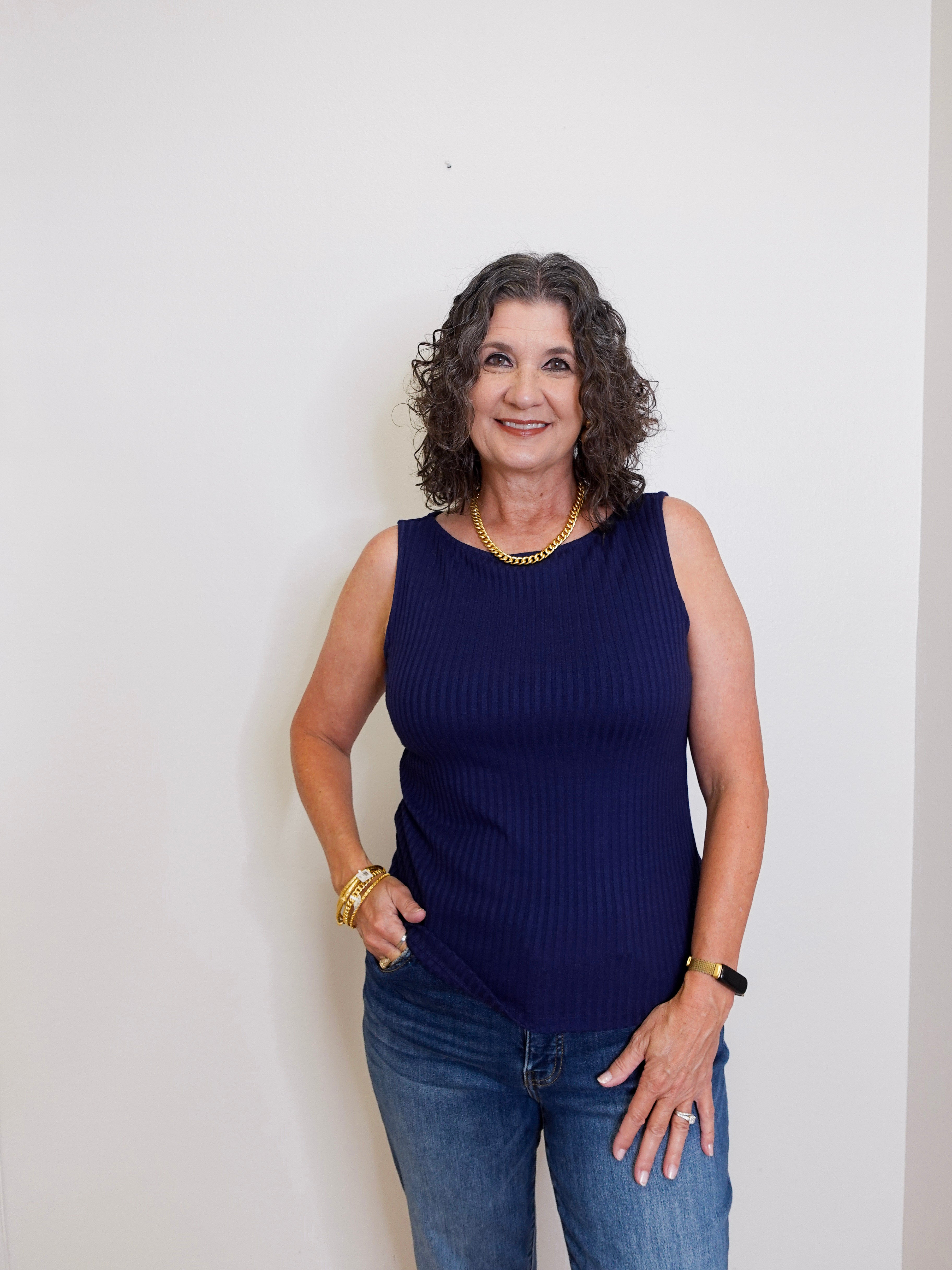 Woman wearing a navy blue sleeveless top and jeans against a white background