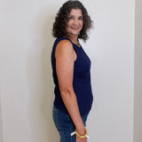 Woman wearing a navy blue sleeveless top and jeans standing against a white wall.
