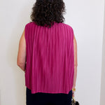 Person wearing a pink pleated top against a white wall