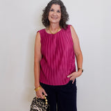 Woman wearing a pink sleeveless top and black pants, holding a leopard print handbag against a white wall.