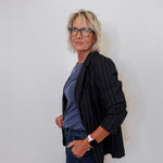 Person wearing a black pinstripe blazer over a blue shirt and jeans against a white wall.