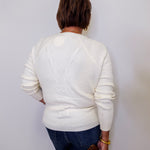 Person wearing a white sweater and blue jeans against a plain background
