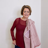 Woman wearing a red top and blue jeans with a pink scarf against a white wall