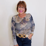 Woman wearing a floral long-sleeve top and jeans against a white wall