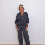 Woman wearing a dark gray outfit standing against a white wall.