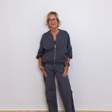 Woman wearing a dark gray outfit standing against a white wall.