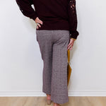 Person wearing a dark brown sweater with lace sleeves and patterned pants against a white wall.