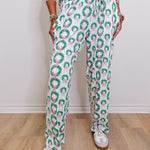 Person wearing a green and pink patterned outfit with white sneakers on a wooden floor.