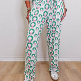 Person wearing a green and pink patterned outfit with white sneakers on a wooden floor.