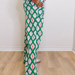 Person wearing green patterned pants with white sneakers on a wooden floor.