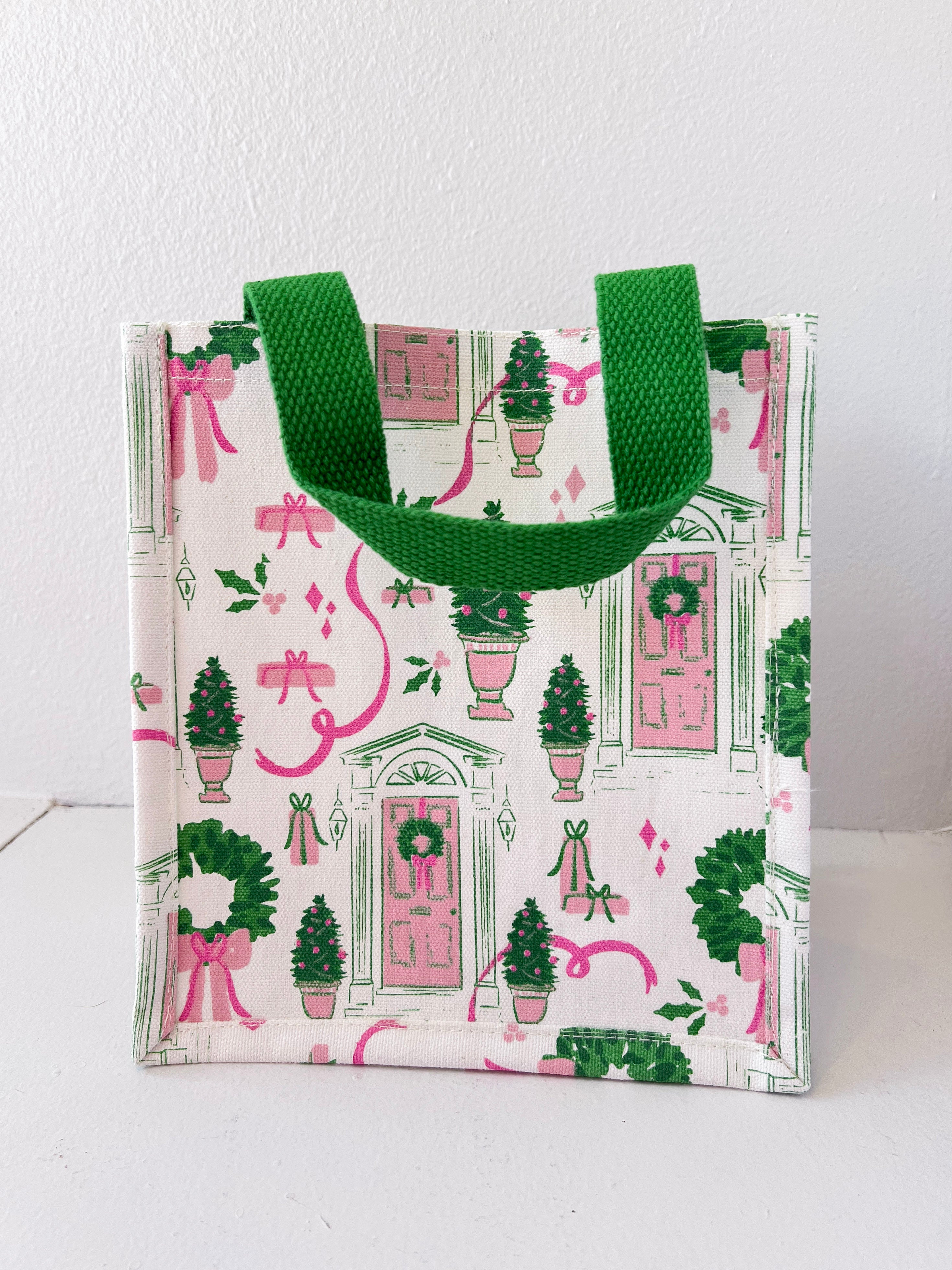 Small tote bag with festive design featuring green trees, pink ribbons, and wreaths on a white background.