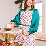 Woman in a kitchen pouring wine, wearing a patterned apron.