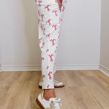 Person wearing white pants with red patterns and white sneakers on a wooden floor.
