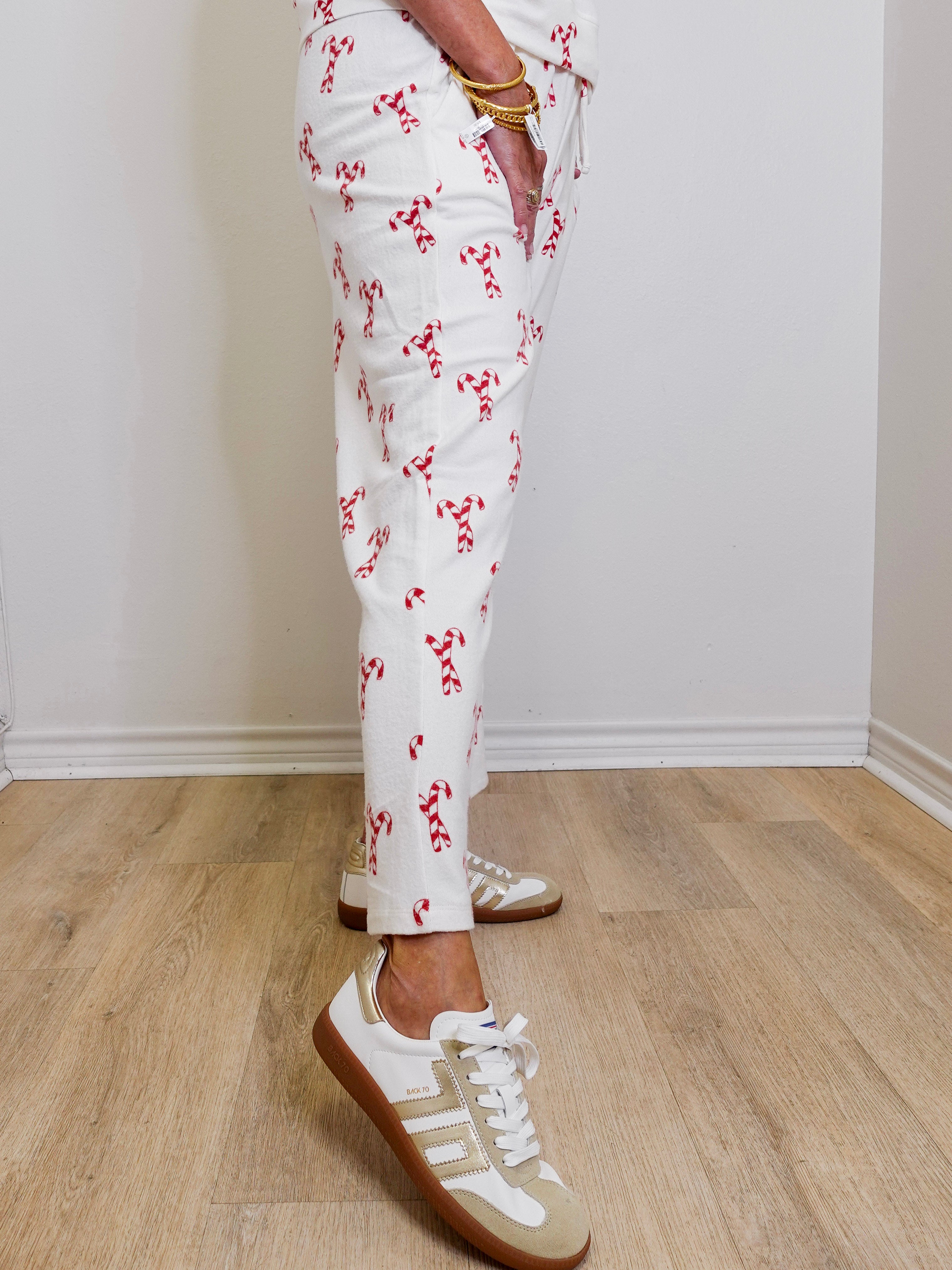 Person wearing white pants with red patterns and white sneakers on a wooden floor.