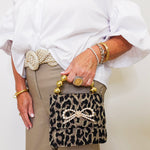 Person holding a leopard print handbag with decorative bow and gold accents.