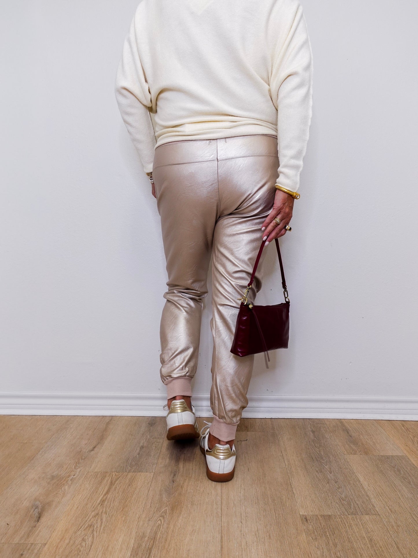 Person wearing metallic pants and a white sweater, standing against a plain wall.