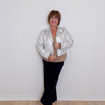 Person wearing a silver jacket and black pants against a white wall.