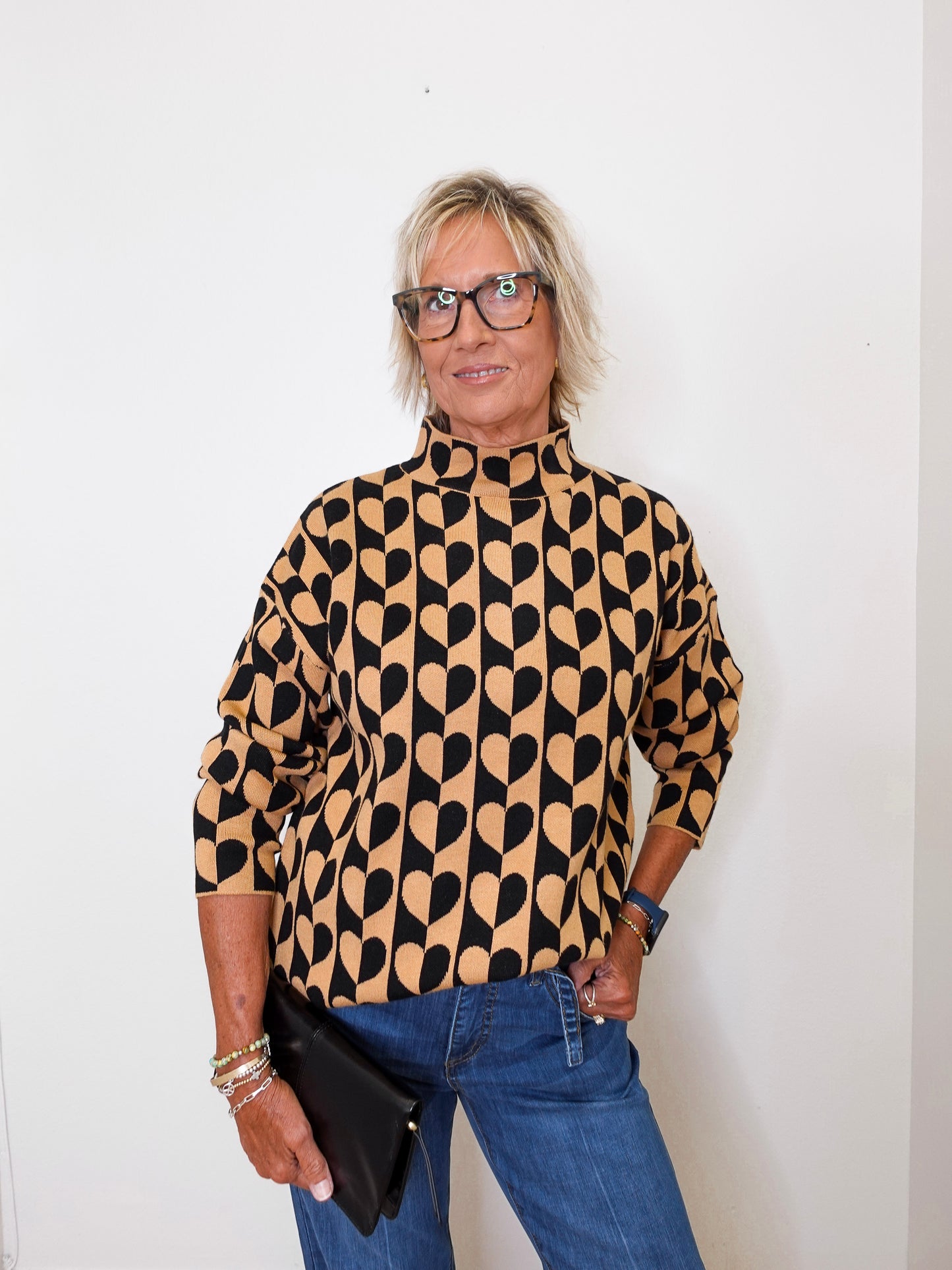 A woman modeling a mock neck heart pattern sweater in front of a white wall.