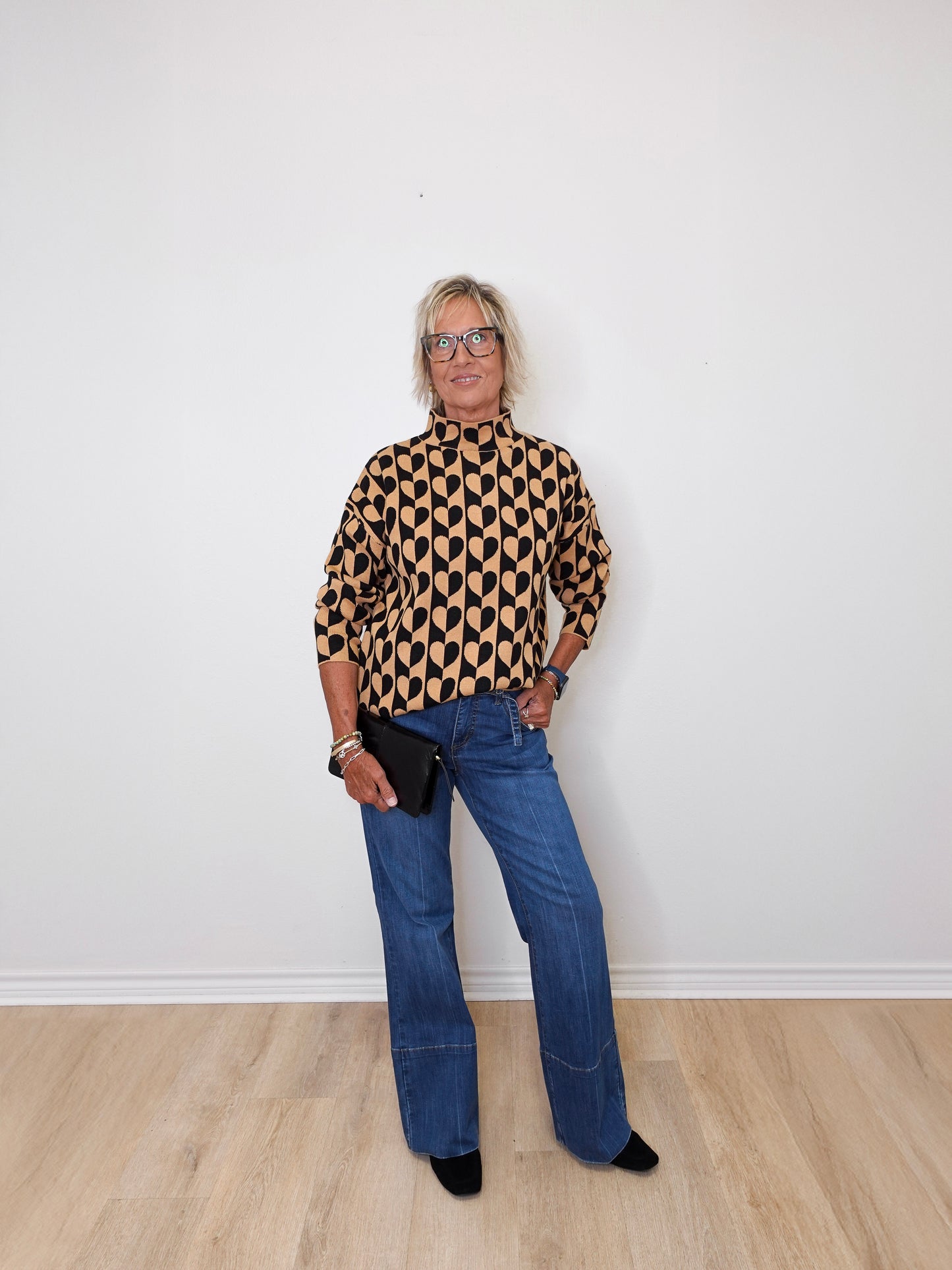 A woman modeling a mock neck heart pattern sweater in front of a white wall.
