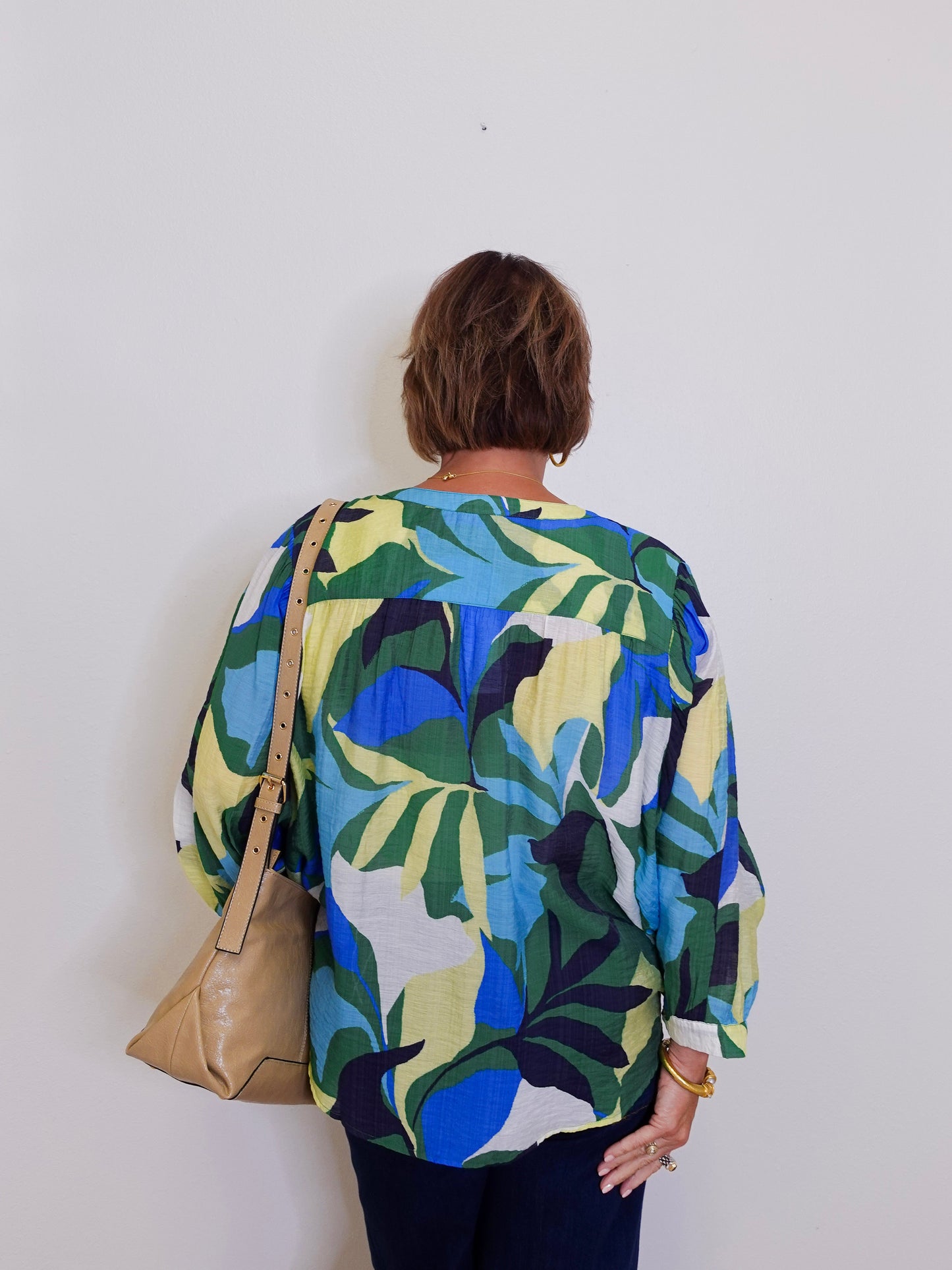 Person wearing a colorful leaf-patterned shirt against a white wall