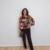Woman wearing a patterned shirt and black pants against a white wall.