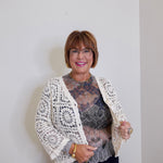 Woman wearing a white lace cardigan over a patterned top against a plain background
