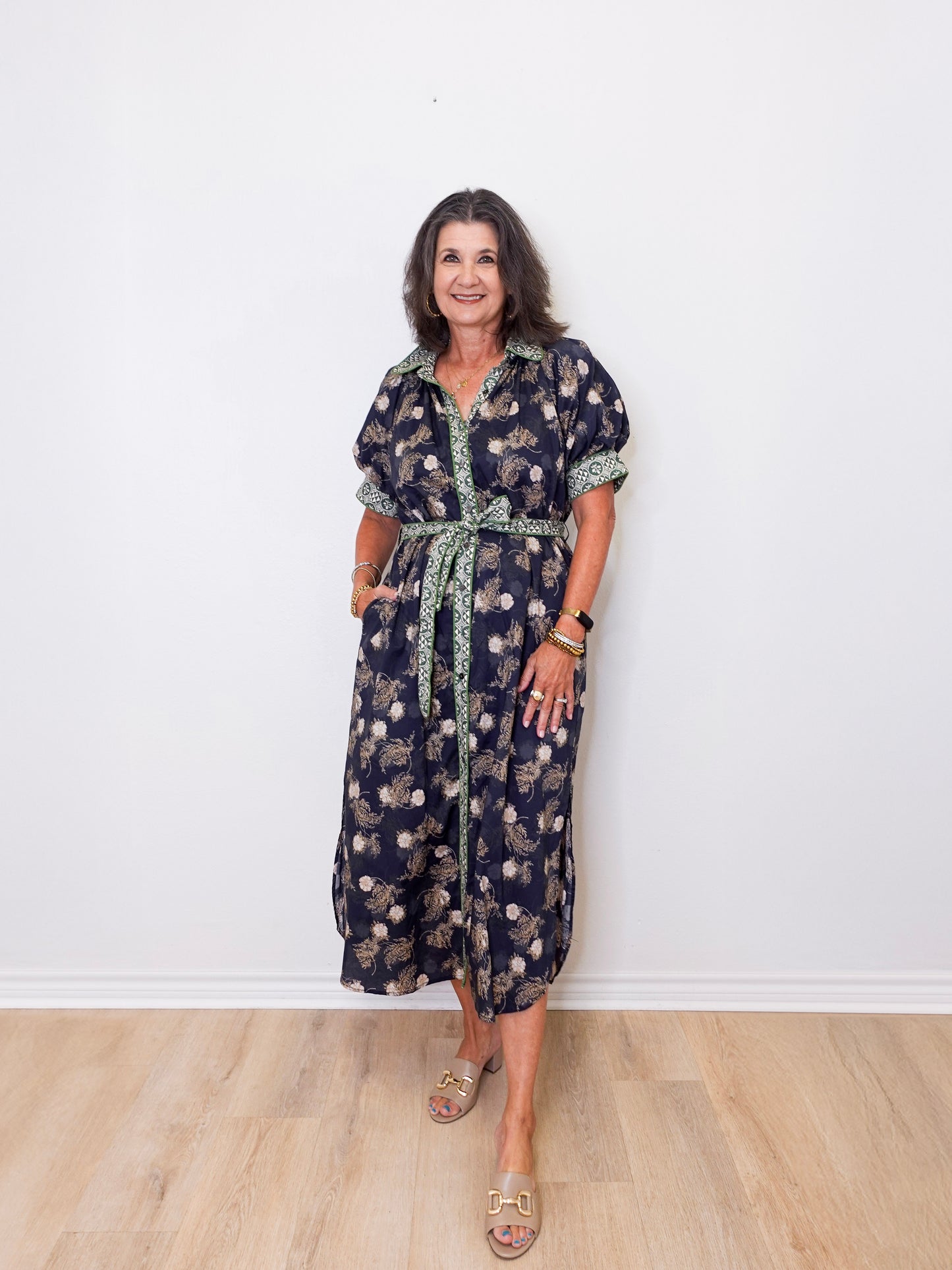 Woman wearing a floral dress standing against a white wall.