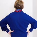 Person wearing a blue outfit with a patterned scarf against a white wall.