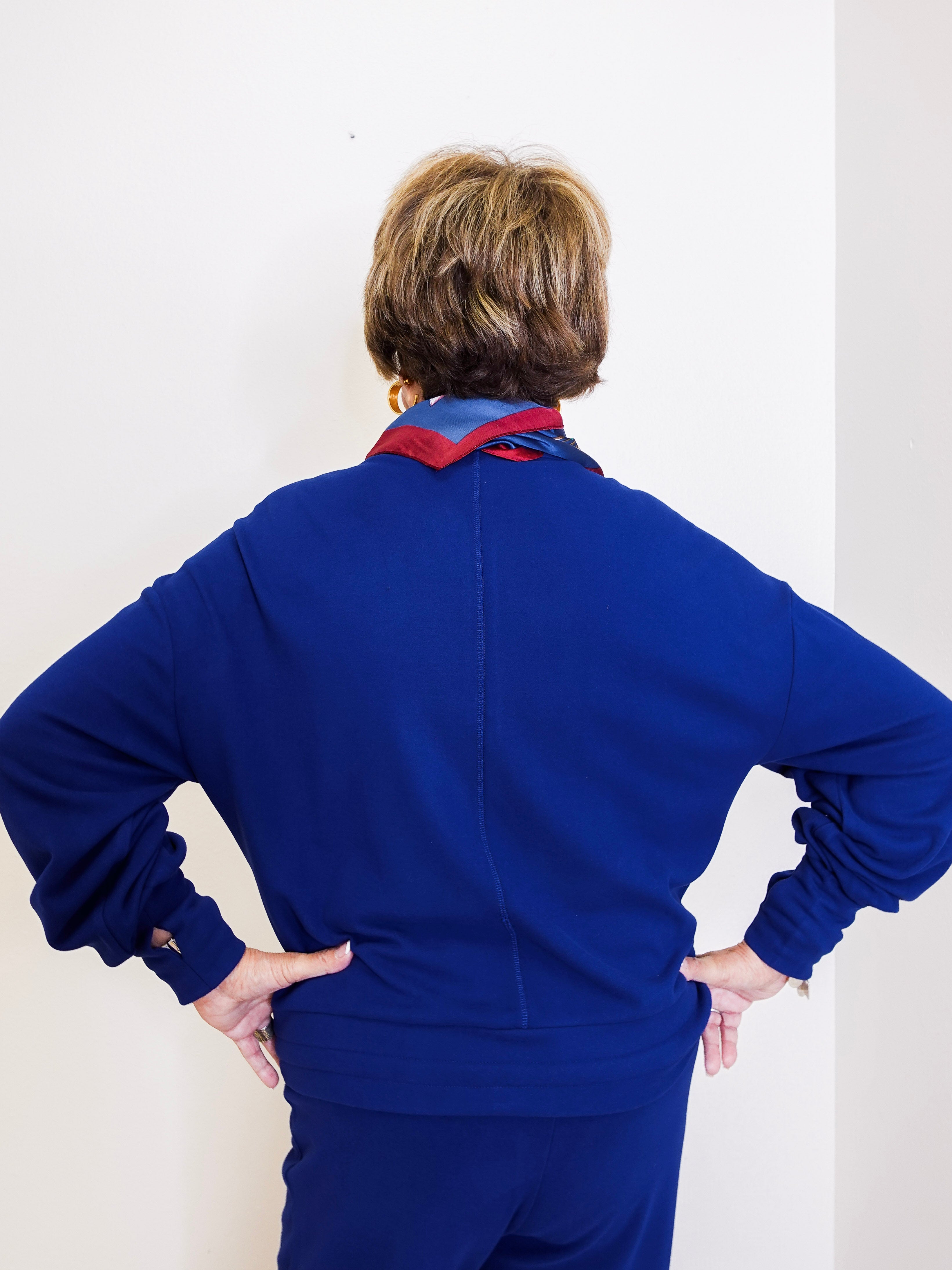 Person wearing a blue outfit with a patterned scarf against a white wall.
