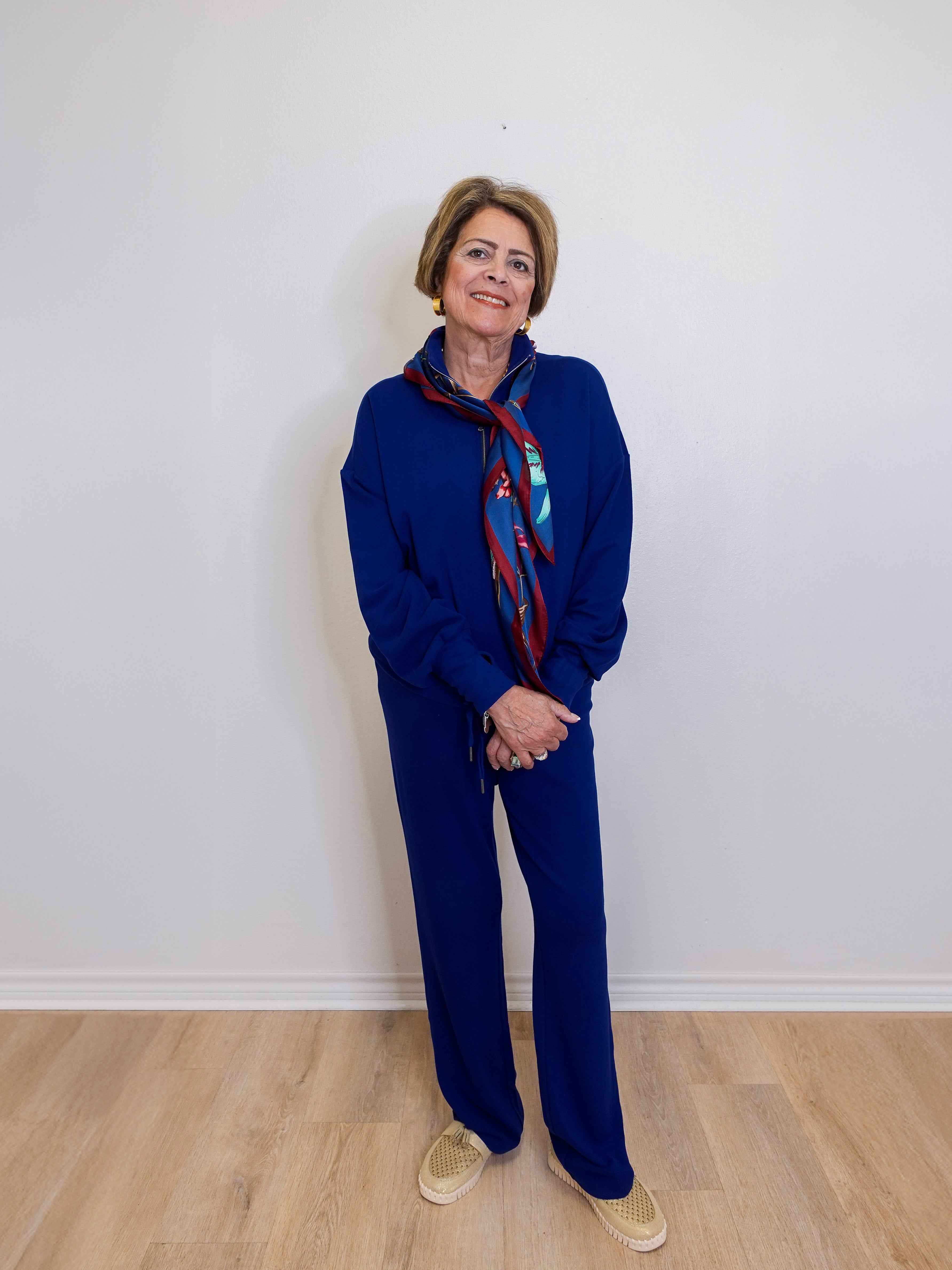 Person wearing a blue outfit with a patterned scarf against a white wall.