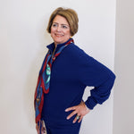 Person wearing a blue outfit with a patterned scarf against a white wall.