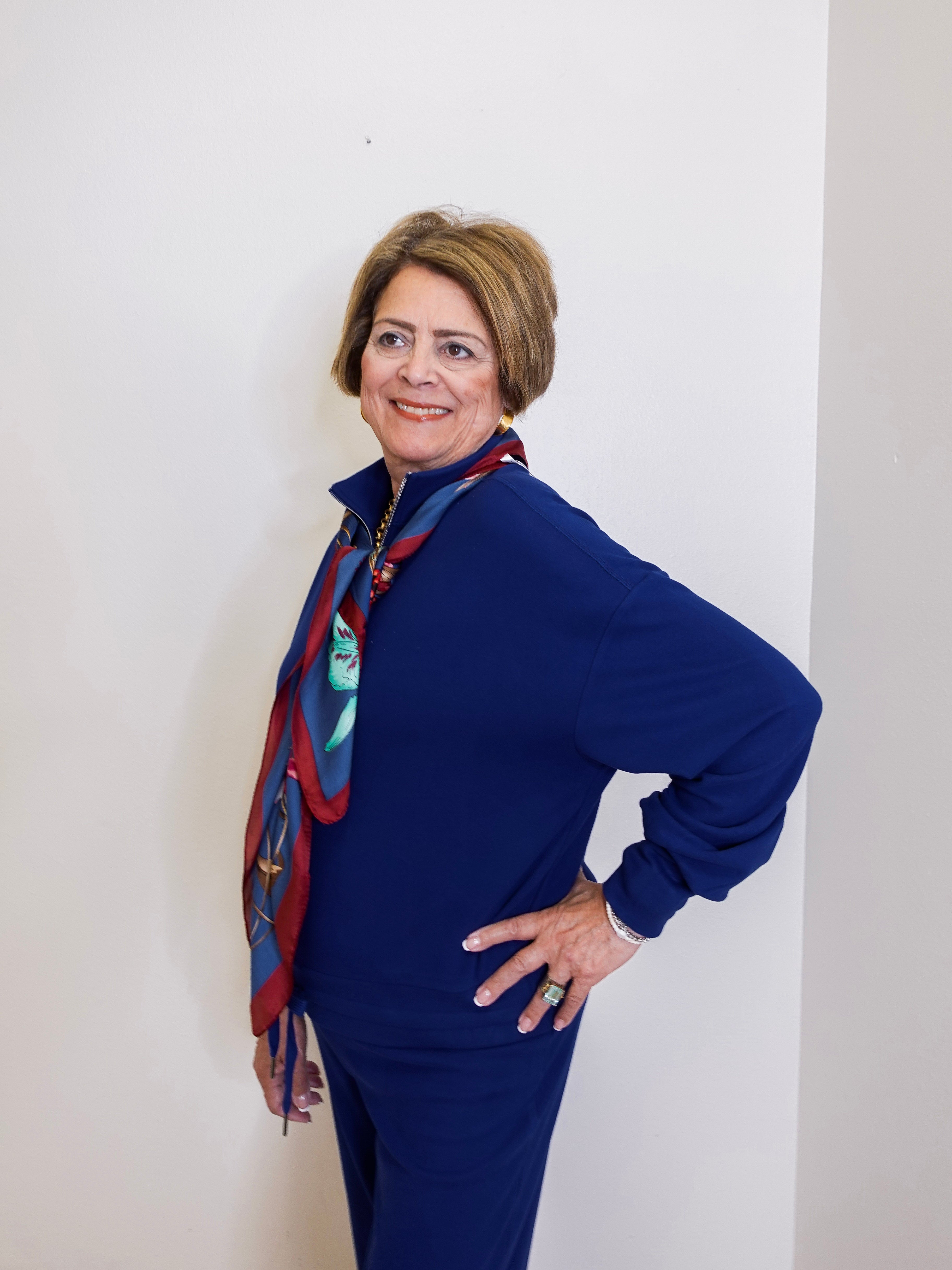 Person wearing a blue outfit with a patterned scarf against a white wall.