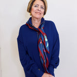 Person wearing a blue outfit with a patterned scarf against a white wall.