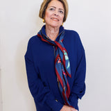 Person wearing a blue outfit with a patterned scarf against a white wall.
