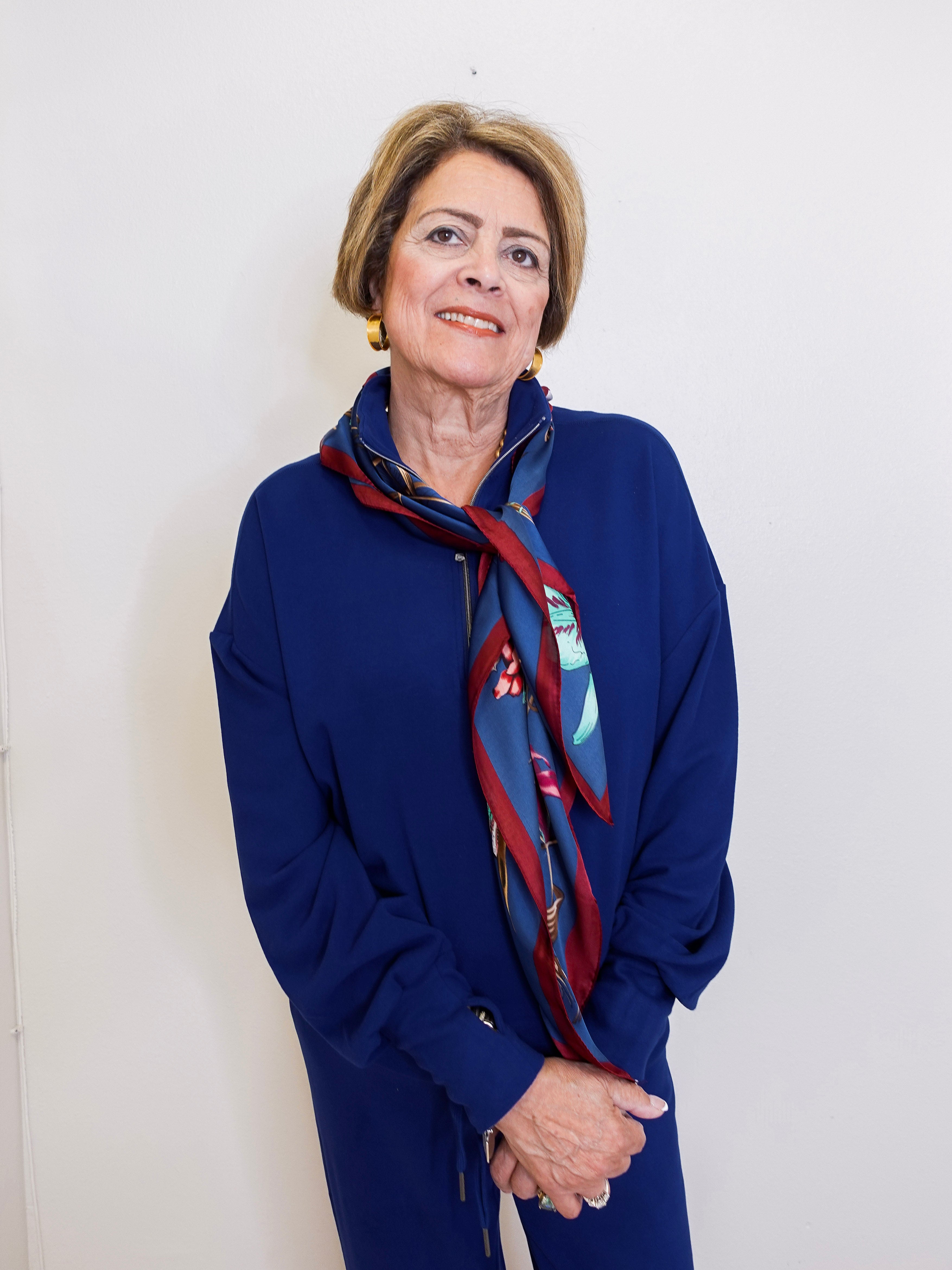 Person wearing a blue outfit with a patterned scarf against a white wall.