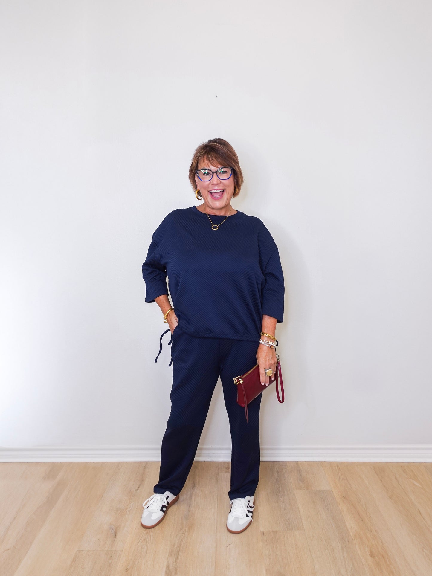 Woman wearing a navy blue outfit with white sneakers against a white wall.