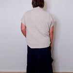 Person wearing a light gray sleeveless top and dark blue skirt against a white wall.