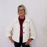 Person wearing a white jacket over a red shirt with a plain background