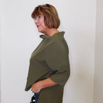 Woman wearing an olive green shirt against a white wall