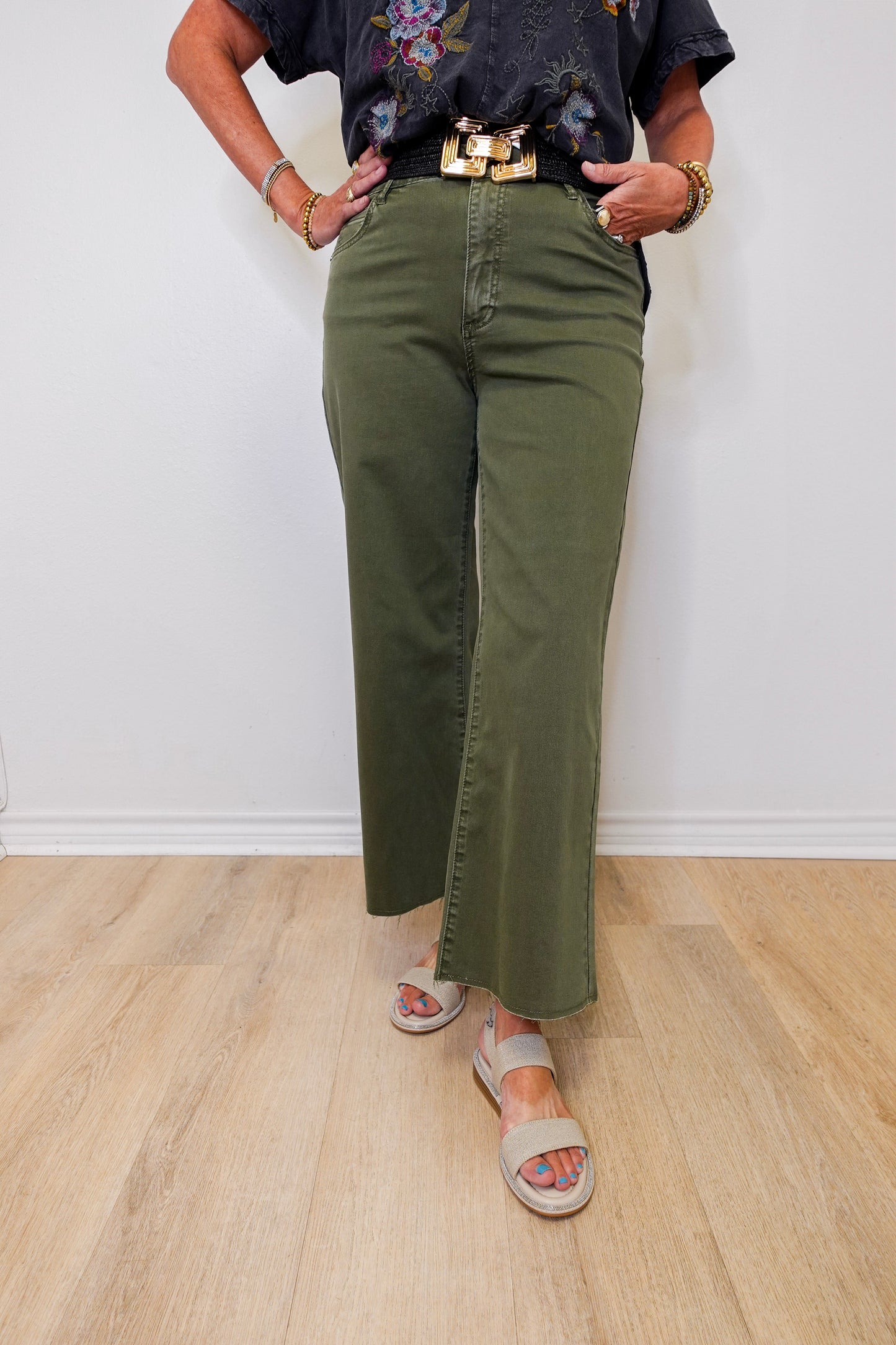 Person wearing green olive green pants and a black top with floral embroidery on a white background