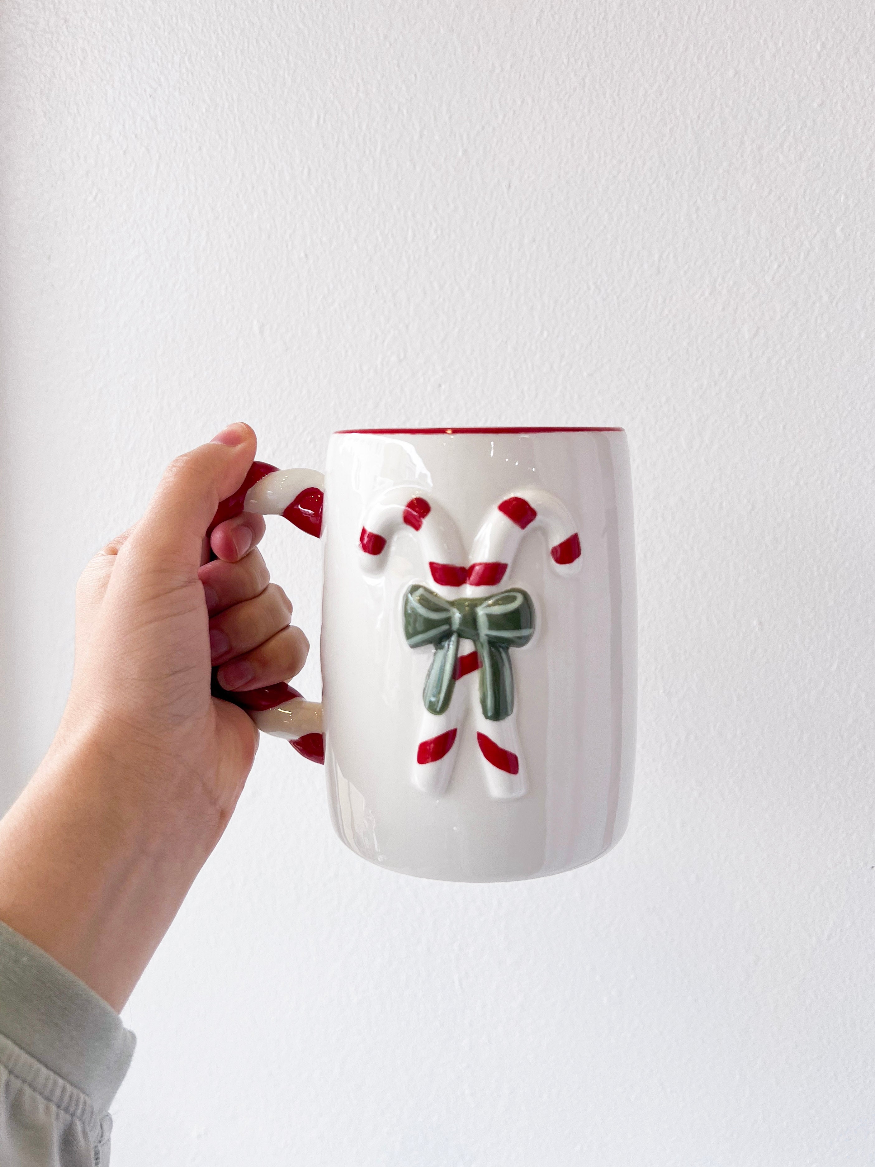 Hand holding a mug with a candy cane design against a white background