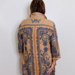 Person wearing a beige coat with blue floral patterns on a white background