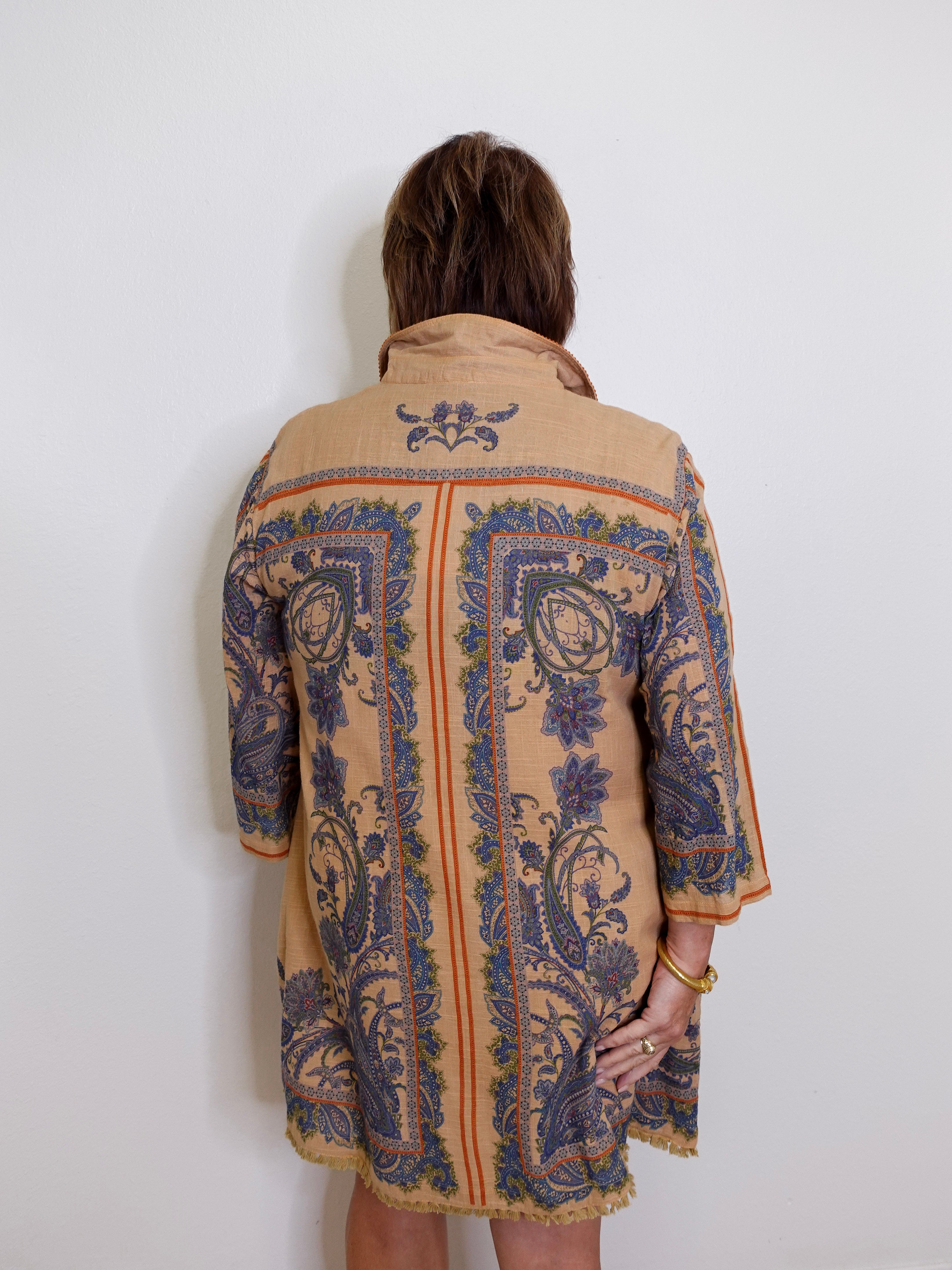 Person wearing a beige coat with blue floral patterns on a white background